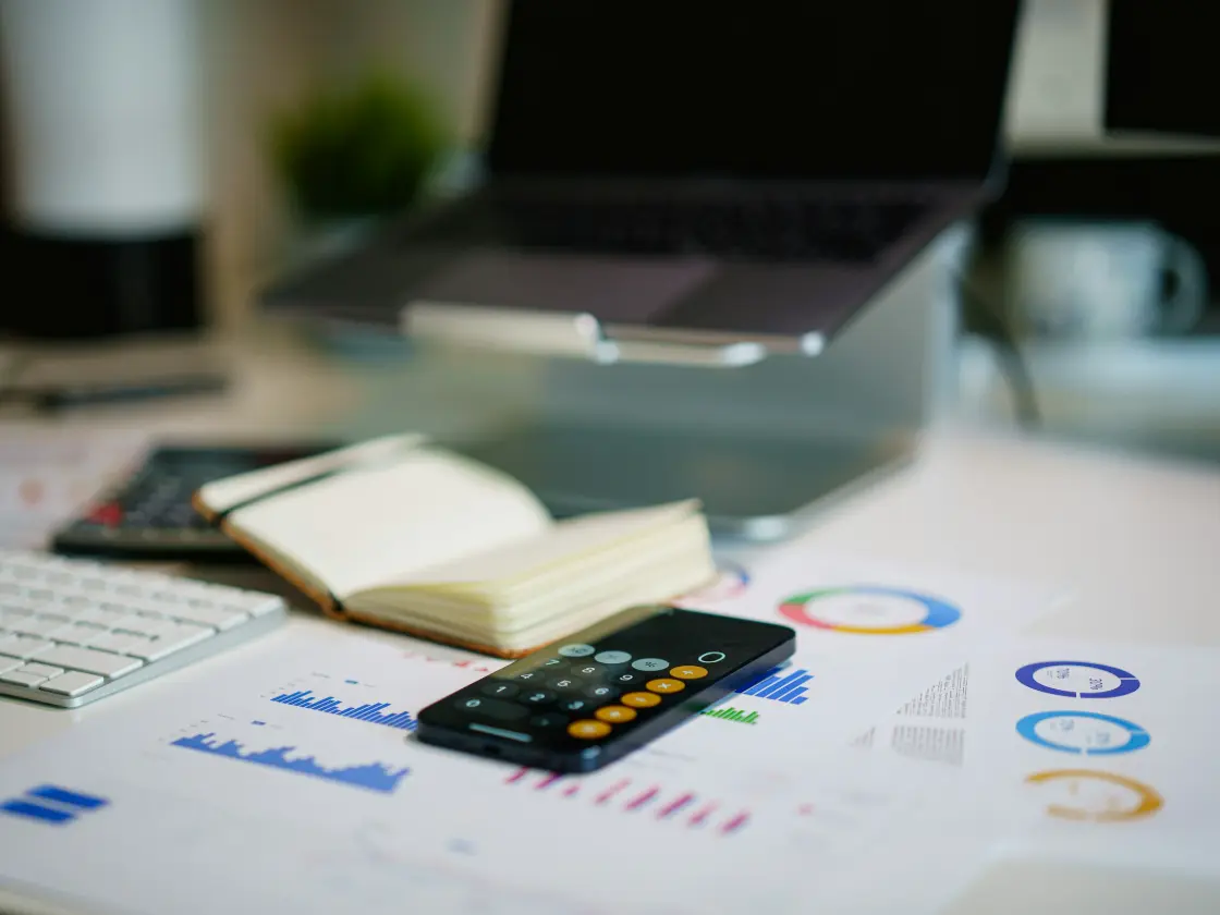 A desk mid-reconciliation: several printed spreadsheets fanned across it, a
                   calculator, a pen resting on a column of figures, and sticky notes on the
                   margins.